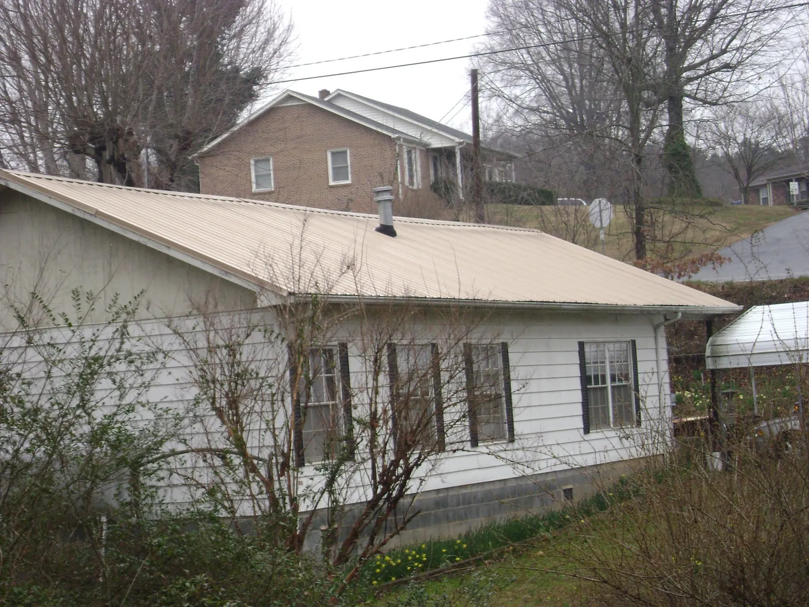 Tan metal roof on a white sided house set into a hillside — Commercial Roofing by Roofing Brothers in Seaford